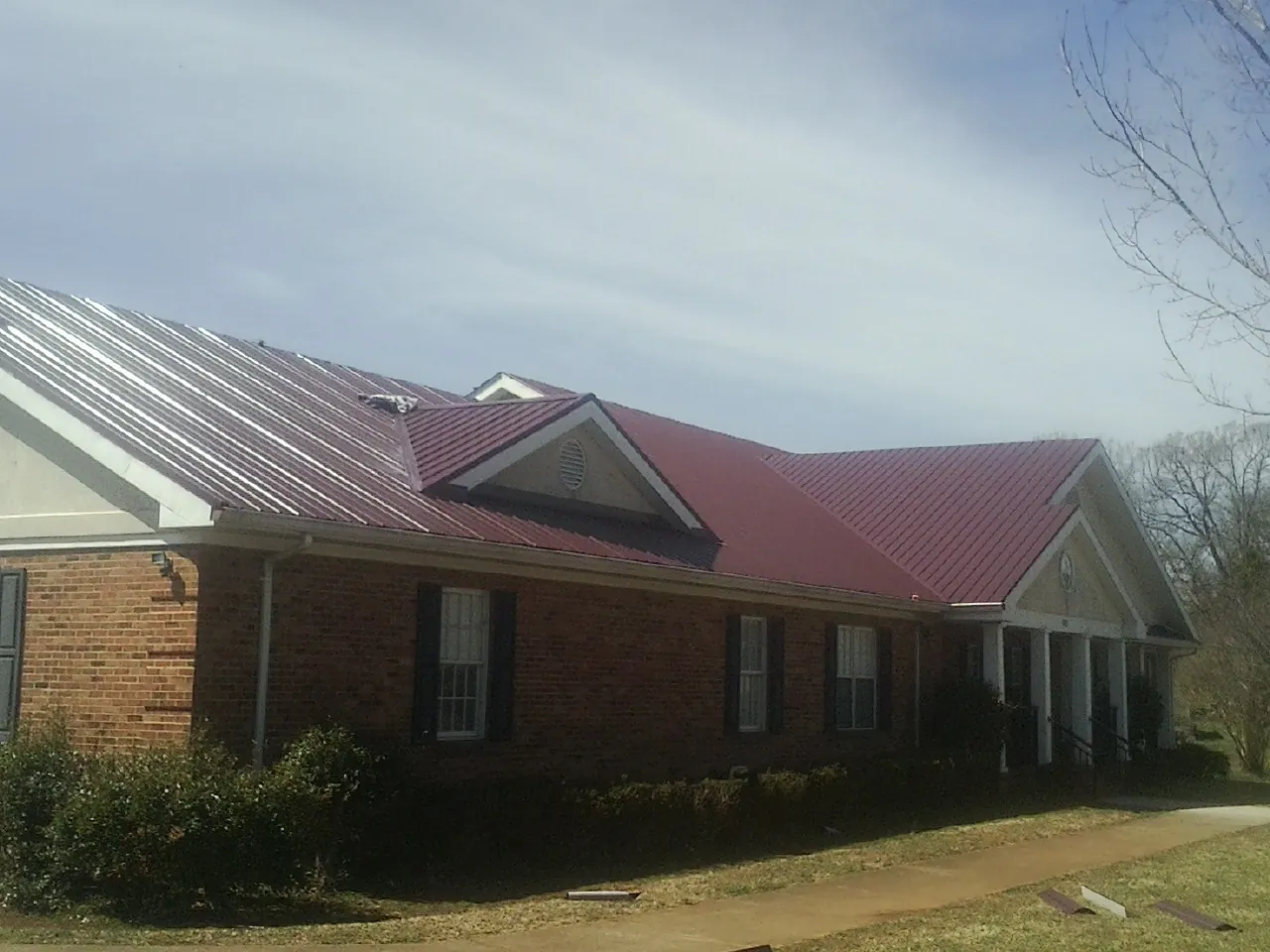 Red metal roof with gabled entries on a long brick building, from a Hail Damage Roof Repair job in Swoope
