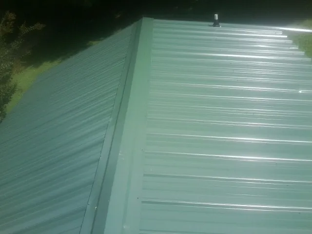 New green metal panels meeting at the ridge of a roof — Flat Roof Repair work by our crew in Swoope