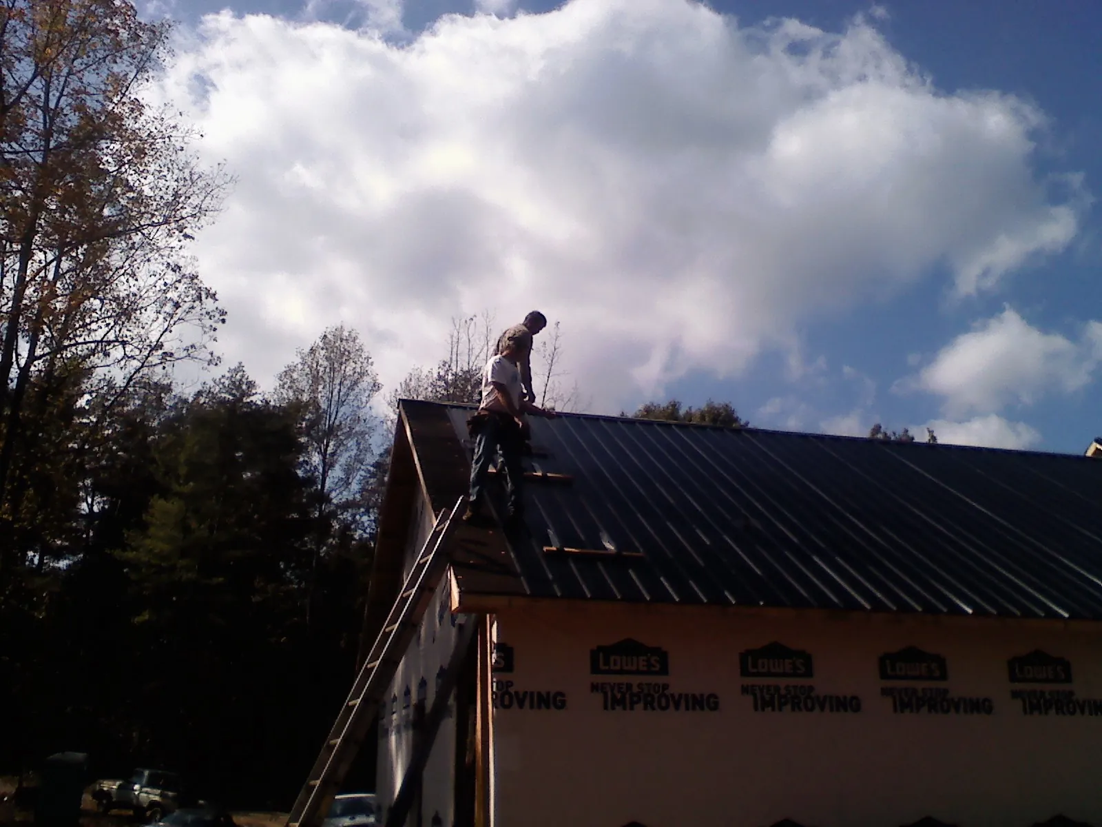 Roofer fastening dark metal panels high against a cloudy sky, from a Roof Inspection job in Swoope
