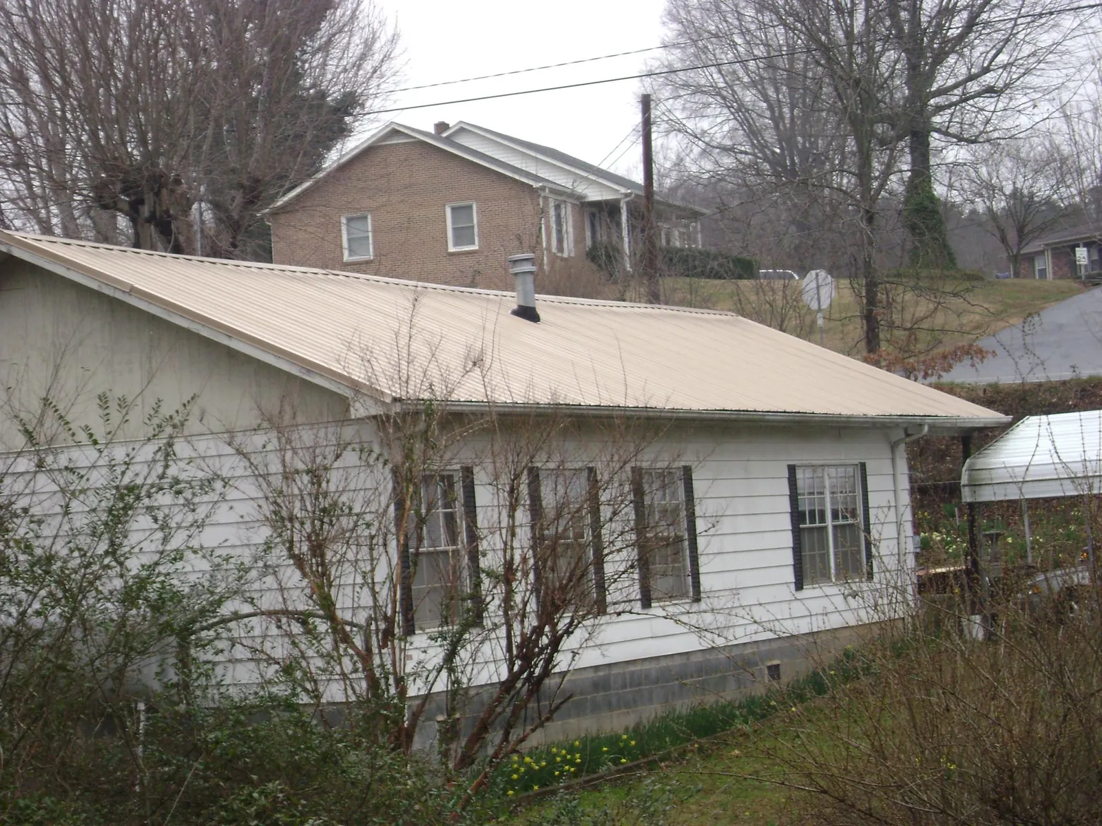 Tan metal roof on a white sided house set into a hillside — Commercial Roofing by Roofing Brothers in Swoope